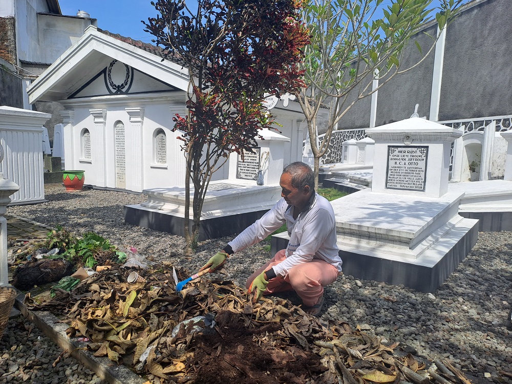Salah satu warga mengumpulkan daun-daun di kompleks Makam Kerkhof di Jalan Ikhlas, Kelurahan Magersari, Kota Magelang, sENIN (1/7/2024).