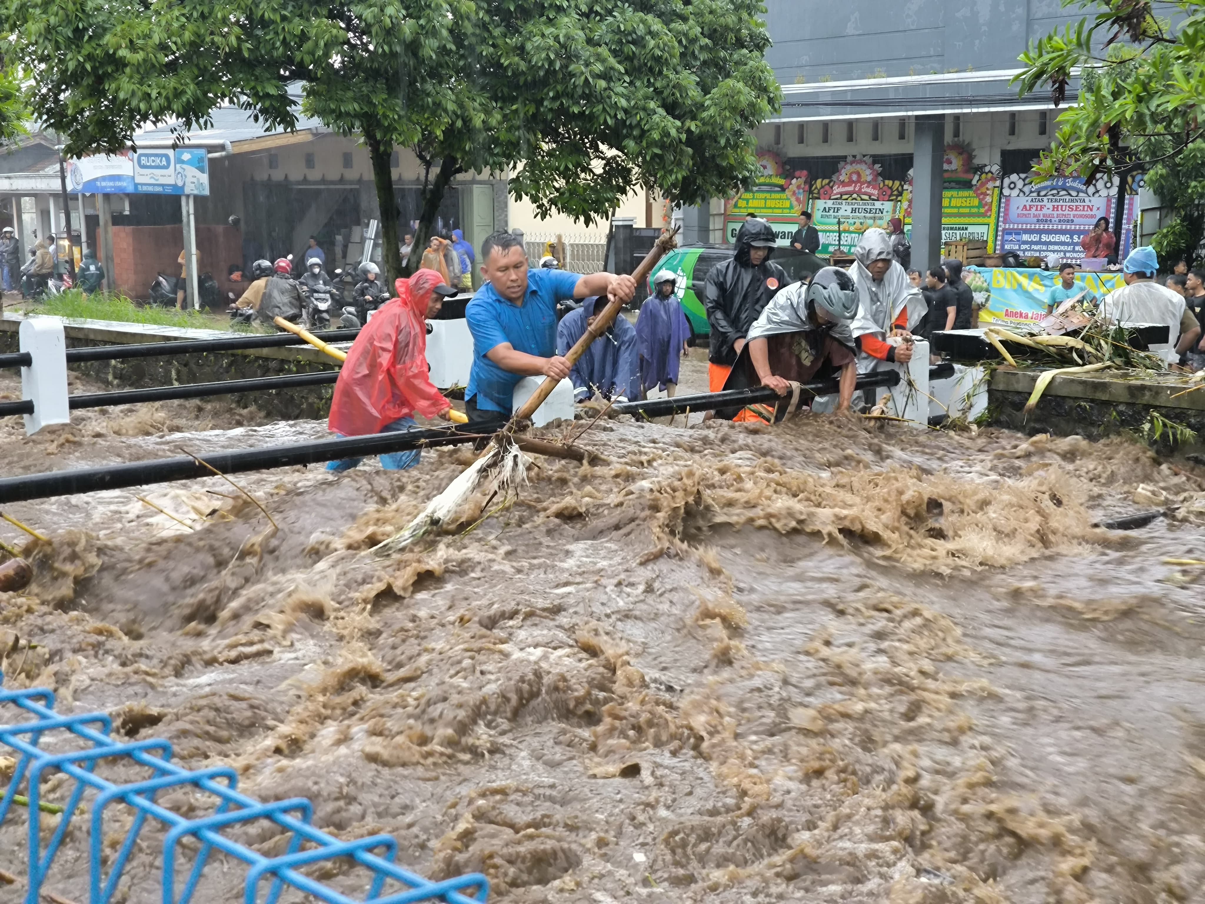 Warga berusaha mengambil sampah di saluran Wangan Aji yang meluap ketika hujan deras kemarin (2/12/2024).