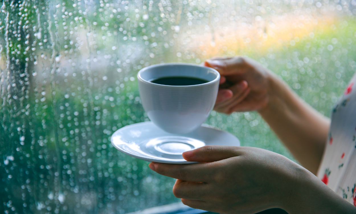 Menikmati segelas kopi hangat sembari menunggu hujan reda di rumah