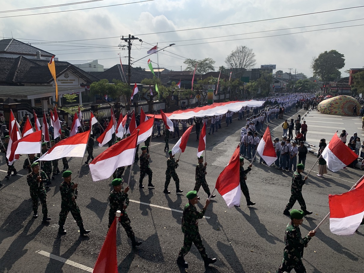 Para pelajar membentangkan bendera merah putih ukuran 30 x 11 meter di jalanan menuju Alun-alun Temanggung, Minggu (10/8/2025).