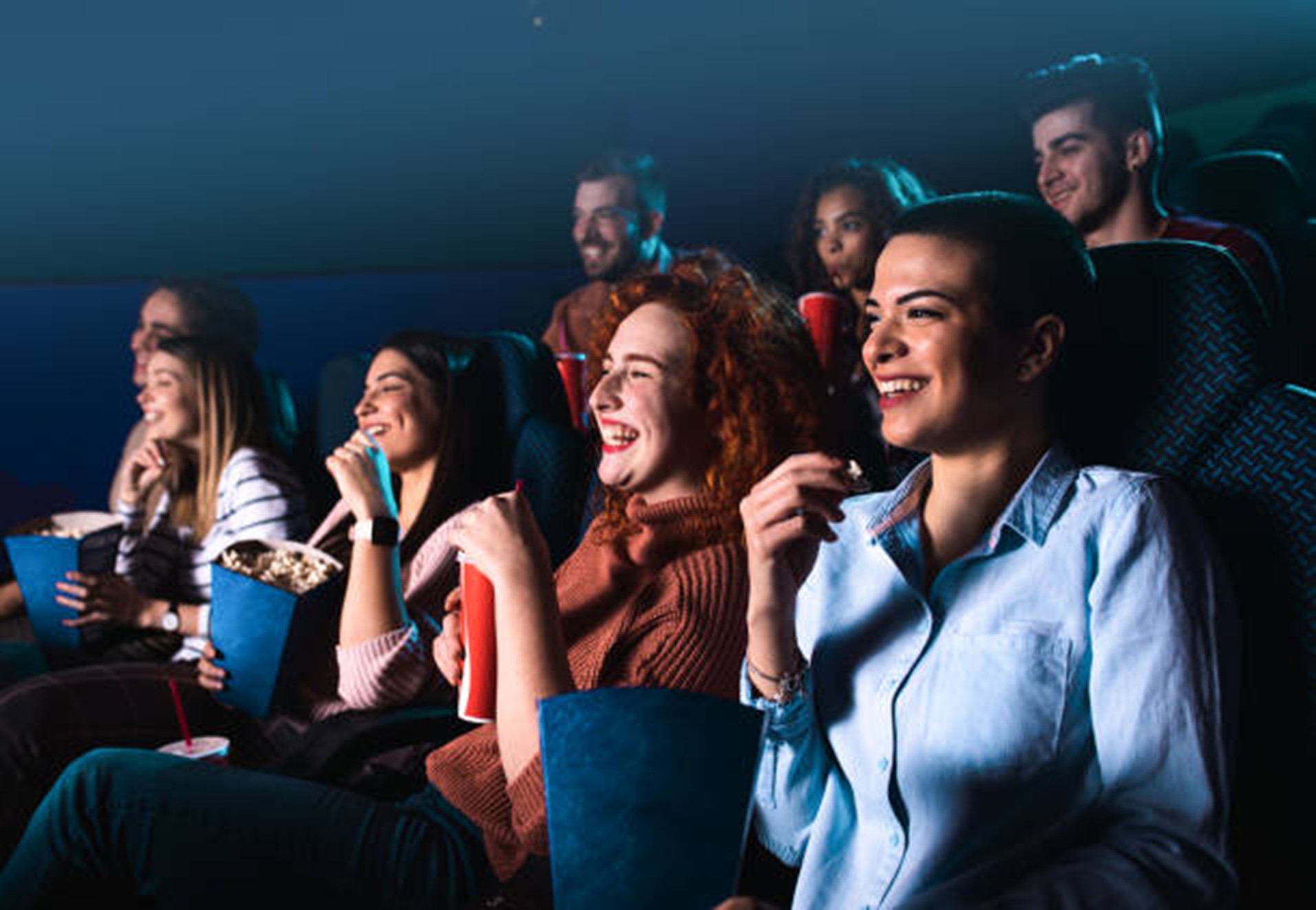 Sekelompok orang ceria tertawa saat menonton film di bioskop.