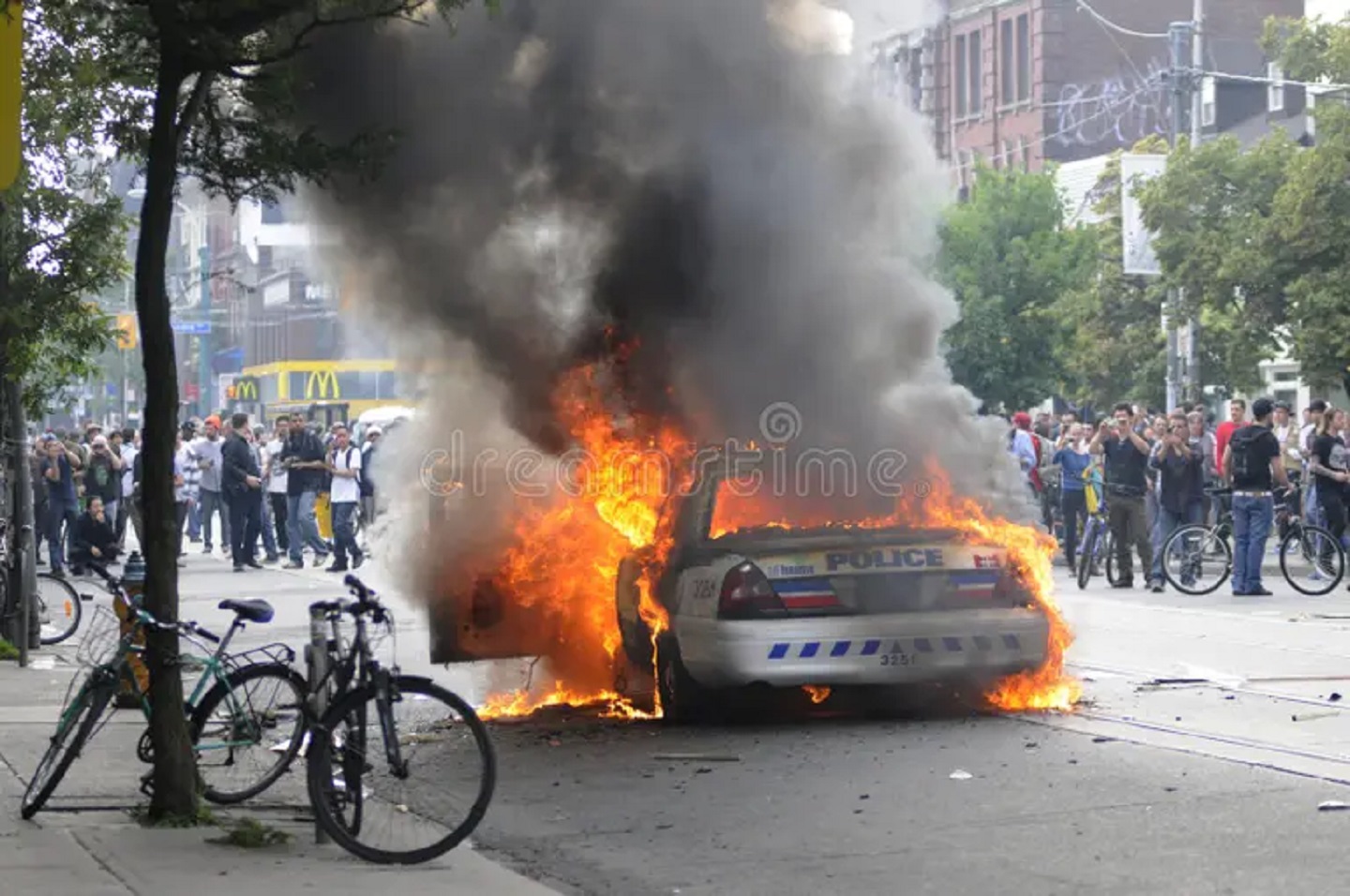 Mobil polisi terbakar di persimpangan Queen dan Spadina sementara para pengunjuk rasa berkumpul di sekitarnya selama Protes G20 pada 26 Juni 2010 di Toronto, Kanada