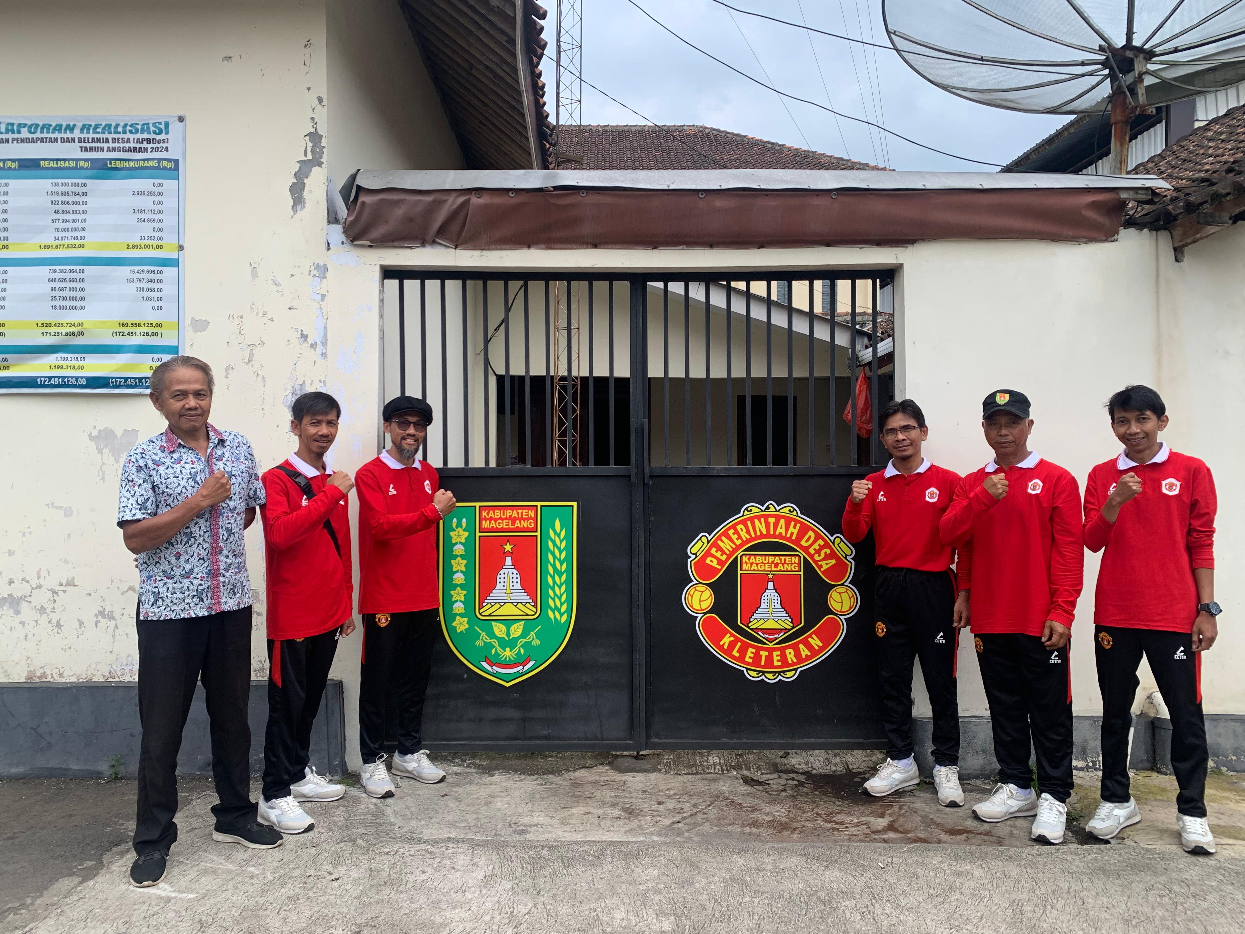 Para Perangkat Desa Kleteran berfoto di gerbang belakang kantor desa dengan menggunakan baju olahraga yang menyerupai seragam MU