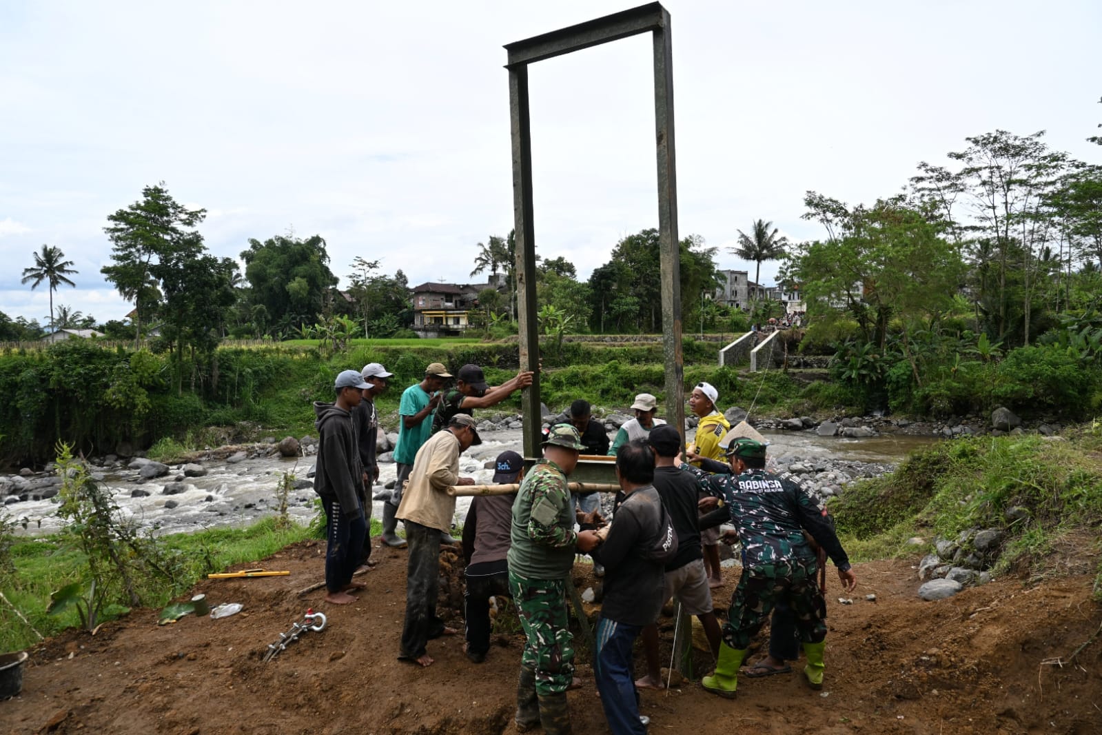 Anggota Kodim 0707 Wonosobo bersama warga memasang tiang pancang jembatan gantung di atas Sungai Begaluh yang menghubungkan Dusun Klilin, Sindupaten dengan Pagentan, Kalikajar.