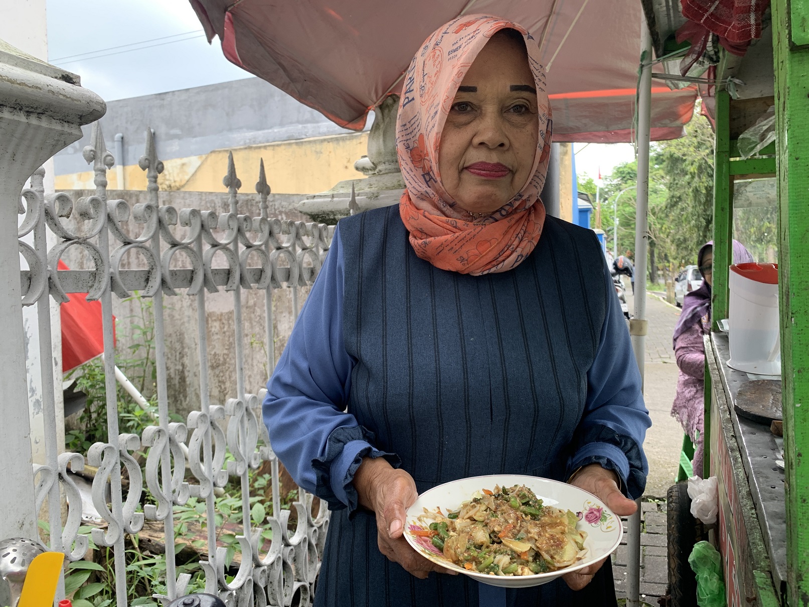 Riniyati dengan sepiring lotek sayur berisi sayuran yang disiram sambal kacang buatannya.