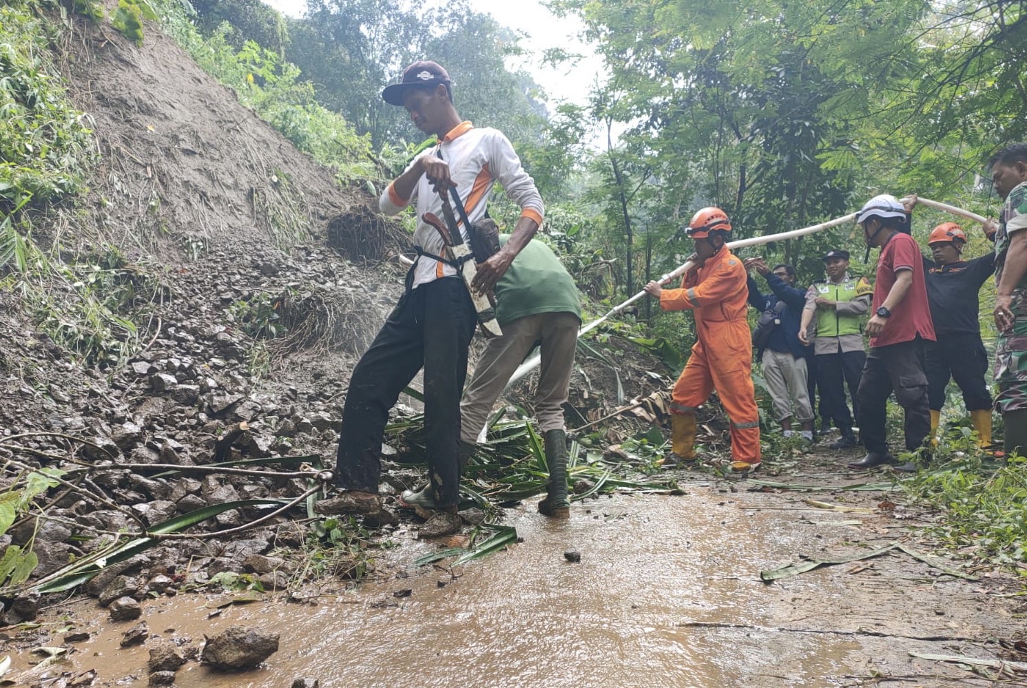 Petugas gabungan gotong-royong membersihkan material longsor yang menutup akses jalan menuju Desa Tlogowungu, Desa Muncar, Gemawang, Minggu (15/2/2026).