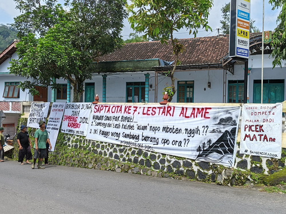 Salah satu spanduk penolakan penambangan tanah urug dipasang warga di depan Kantor Desa Sambeng, Minggu (22/2/2026).
