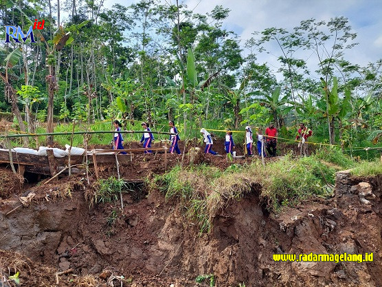 Anak-anak Desa Ngadisepi, Kecamatan Gemawang, Kabupaten Temanggung saat melintasi jalan sementara sebagai pengganti jalan desa yang longsor Rabu (25/1). (ADDIN ALFATH/ JAWA POS RADAR MAGELANG)