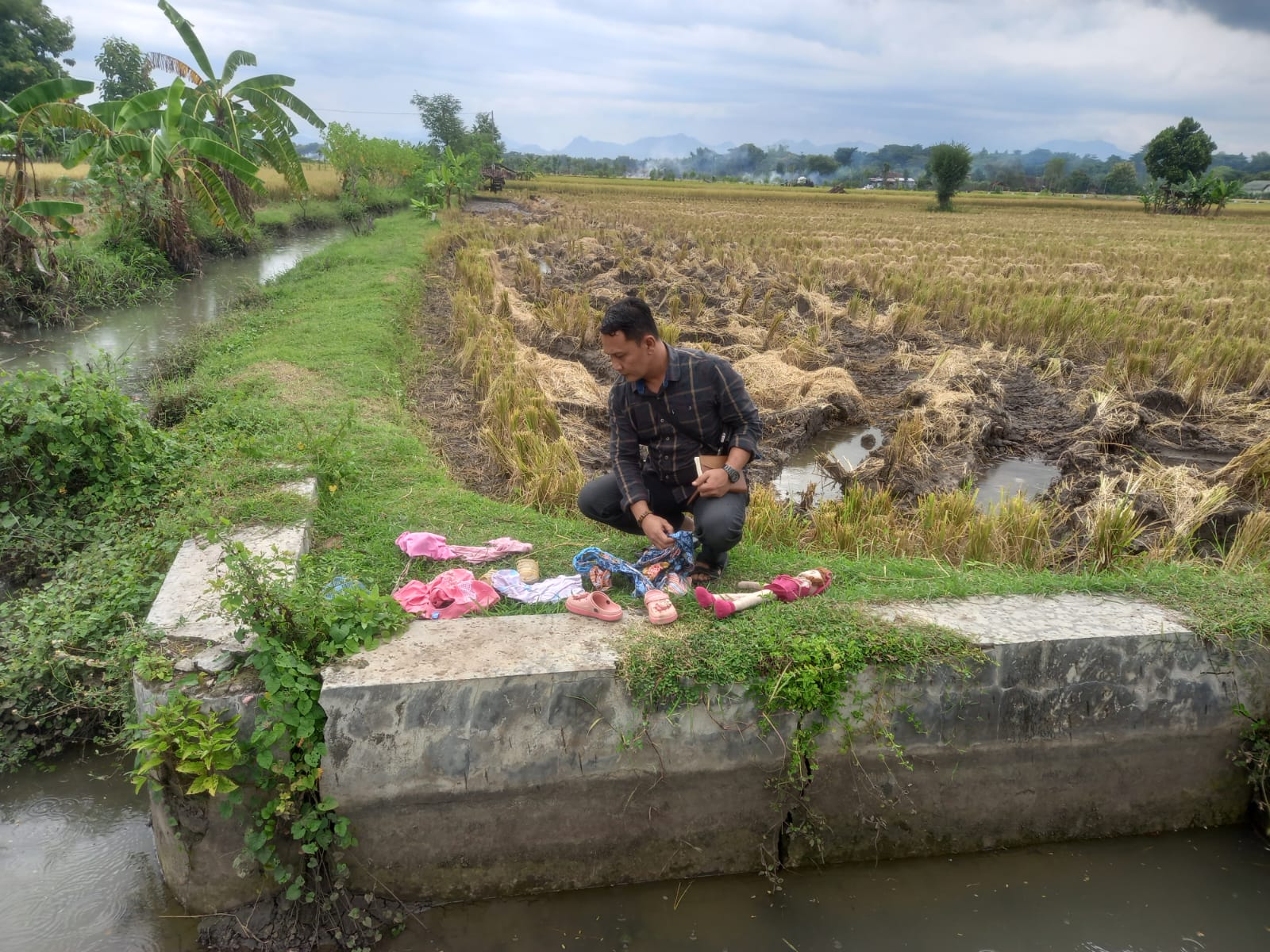 BARANG BUKTI: petugas memeriksa pakaian, boneka dan sandal yang diduga milik kedua bocah yang tewas tenggelam di sungai Setono.