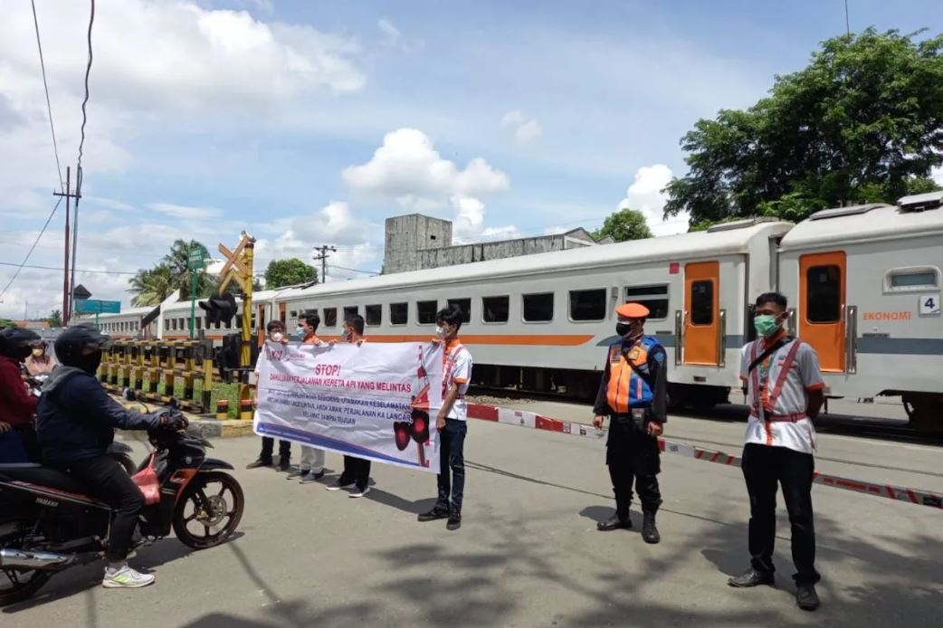 Ilustrasi Petugas KAI mengedukasi pengendara demi keselamatan di perlintasan kereta api.