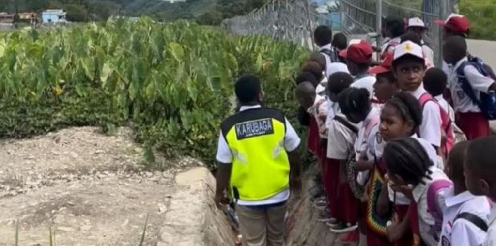 Anak-anak SD di Tolikara, Papua Pegunungan, menunggu pesawat melintas sebelum menyeberang menuju sekolah.