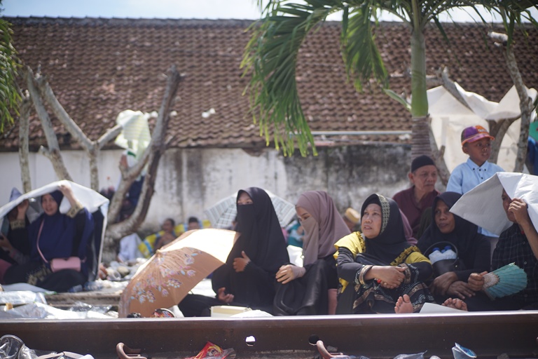 Kondisi peziarah Haul Habib Sholeh yang antusias di tengah terik matahari dan duduk di rel kereta api, Minggu (24/4) (FotoL YULIO/HALOJEMBER - RADARJEMBER - JAWAPOS.COM)