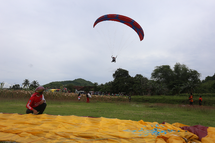 TERBANG: Peserta tandem paralayang hendak mendarat di area Landing Skyland, Kecamatan Wuluhan, Sabtu (30/11). (YULIO FA/RADAR JEMBER)