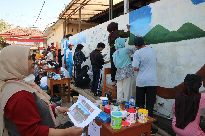 KOMPAK: Para guru dan siswa saling bekerjasama membuat seni mural di tembok luar SMAN Arjasa. Mereka juga menyiapkan sketsa hingga mencampur cat untuk menemukan warna yang diinginkan.