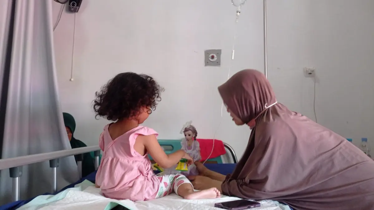 Hasna Wulandari (kanan) mengajak anaknya bermain di sela-sela perawatan seusai diduga keracunan menu MBG di Puskesmas Kaliwates, Kamis (21/5/2026). (Sidkin Ali/Halojember)