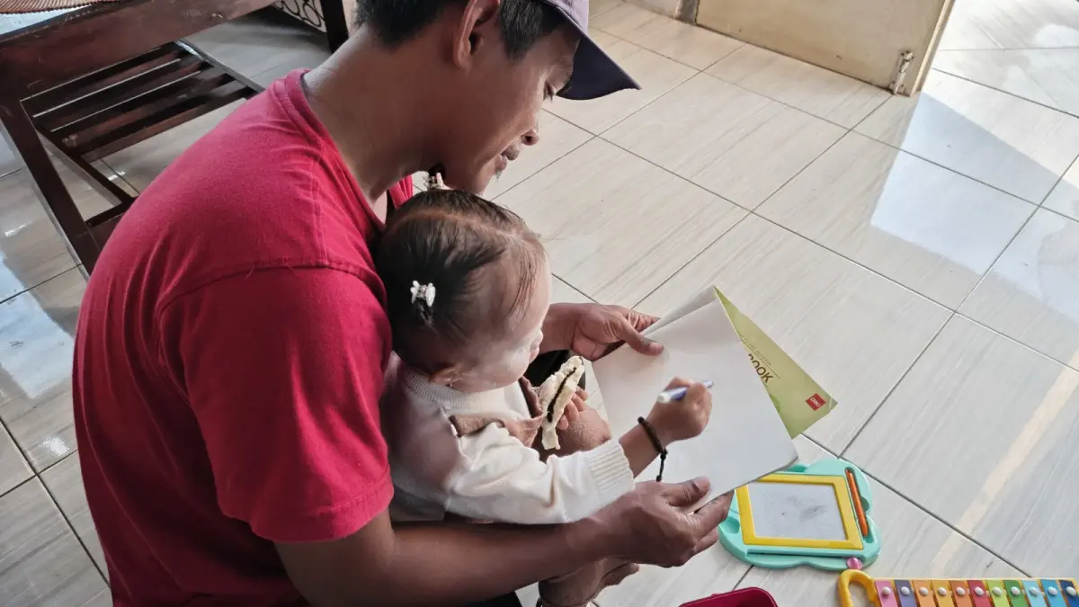 MENGAJARI: Ali Arizan saat mengajari sang anak cara menulis di rumahnya. (FAQIH HUMAINI/HALOJEMBER)
