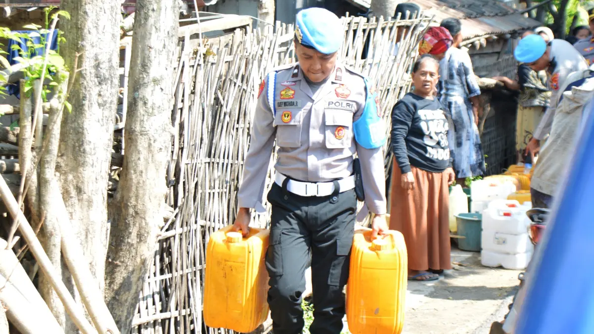 DIBANTU: Salah satu anggota Polres Bondowoso membawakan air bersih ke rumah warga, dengan wadah yang sudah disiapkan sebelumnya. (ILHAM WAHYUDI/HALO JEMBER)