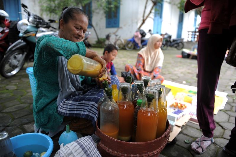 Penjual jamu gendong sedang meracik jamu pesanan pelanggan. Sebagai minuman herbal, Jamu sah menjadi warisan budaya tak benda dari UNESCO.