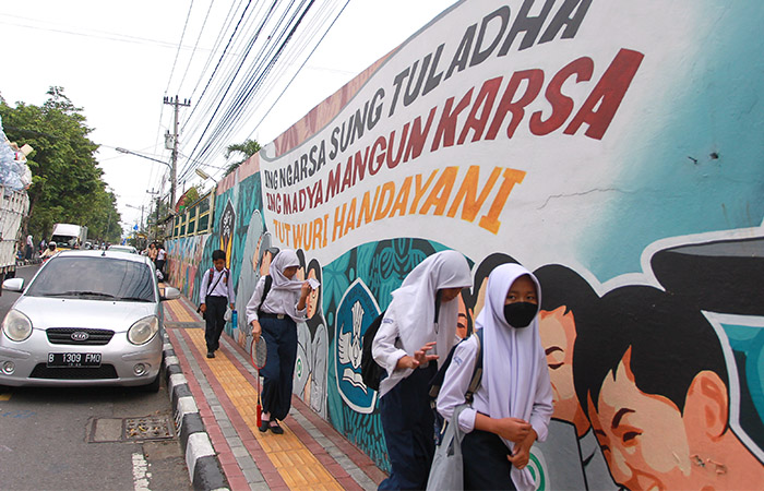 PULANG SEKOLAH: Pelajar tingkat SMP melintas di depan mural bergambar Ki Hajar Dewantara dan tiga semboyannya di Jalan Ngeksigondo, Kotagede, Jogja kemarin (10/1).