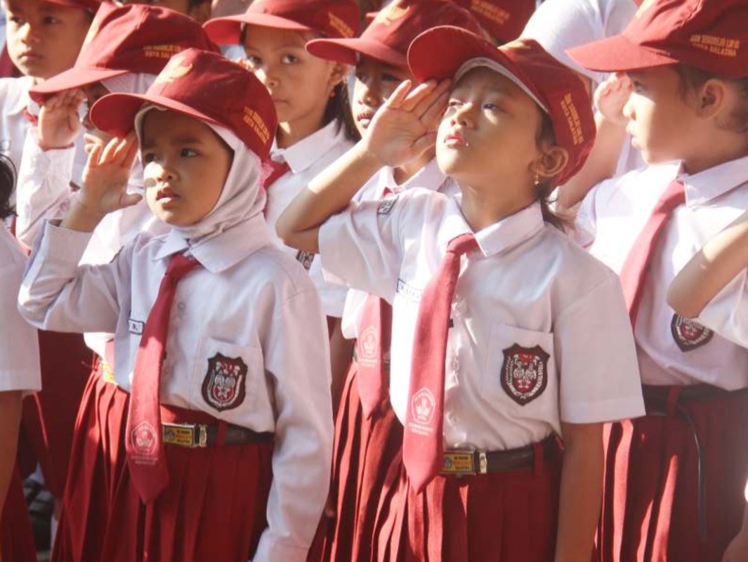 Potret murid sekolah dasar mengenakan seragam putih-merah sedang mengikuti upacara bendera. (Wikimedia Commons/Public Domain)