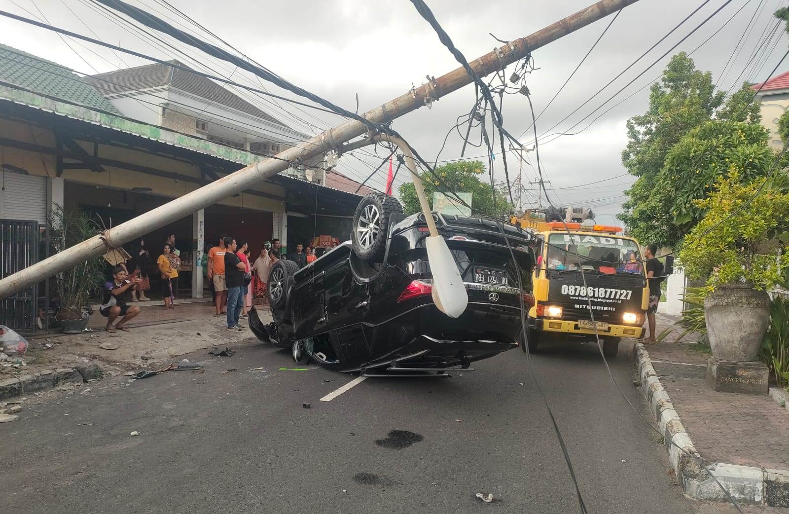 TERBALIK: Toyota Fortuner warna hitam tampak terbalik setelah pengemudinya menabrak tiang listrik karena menghindari kucing di Denpasar, Bali.