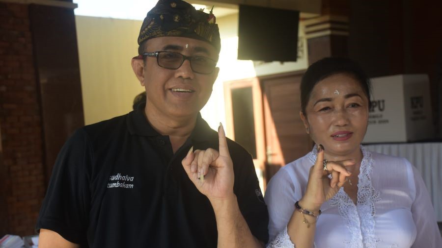 HAK PILIH: Walikota Jaya Negera didampingi istri keluar dari bilik suara di TPS 17 Penatih, Denpasar Timur, Rabu (14/2).