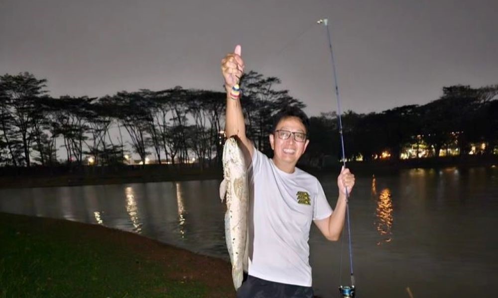 IKAN JUMBO: Tung Desem Waringin memamerkan ikan tangkapan di danau buatan belakang rumahnya.