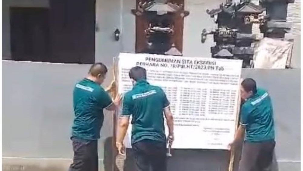 SITA EKSEKUSI: Petugas PN Tabanan memasang papan sita eksekusi obyek HT nasabah KSP EDM, Setiawati di Denbatas, Tabanan.