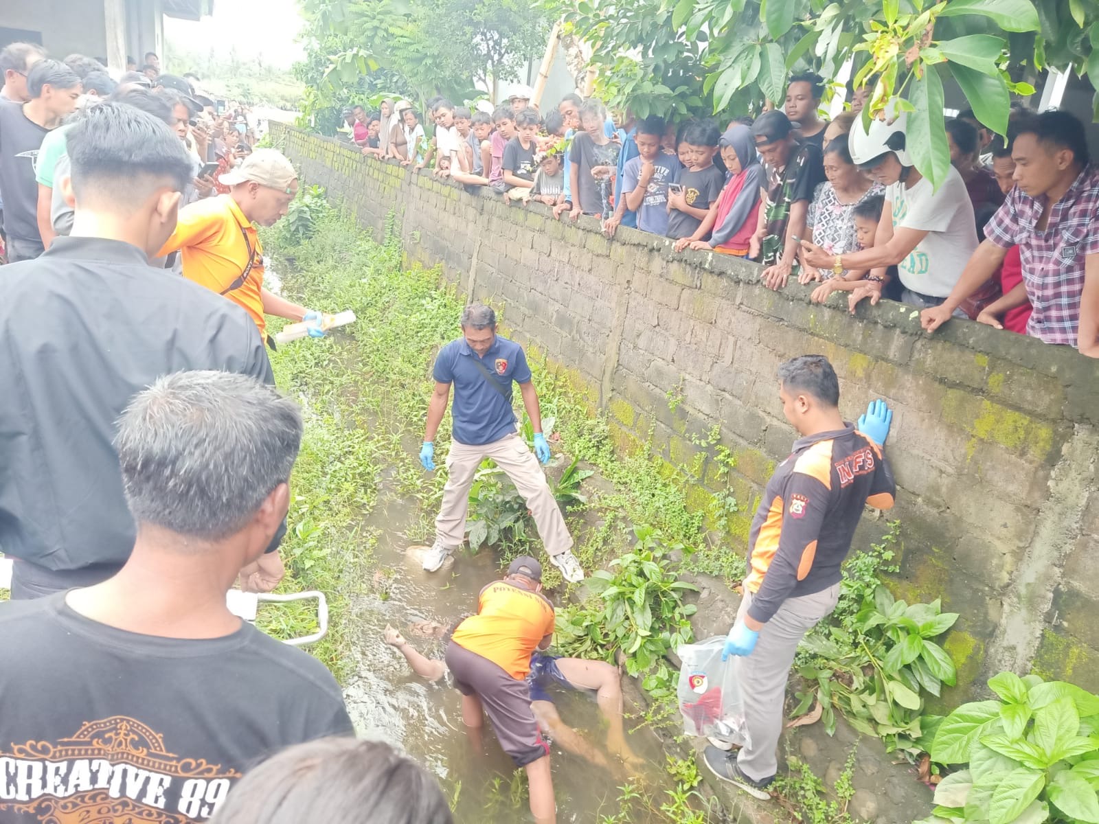OLAH TKP : Warga terlihat memadati lokasi penemuan jenazah PY di saluran irigasi utara pertigaan Desa Yehkuning, Kecamatan Jembrana, Selasa (10/12/2024).
