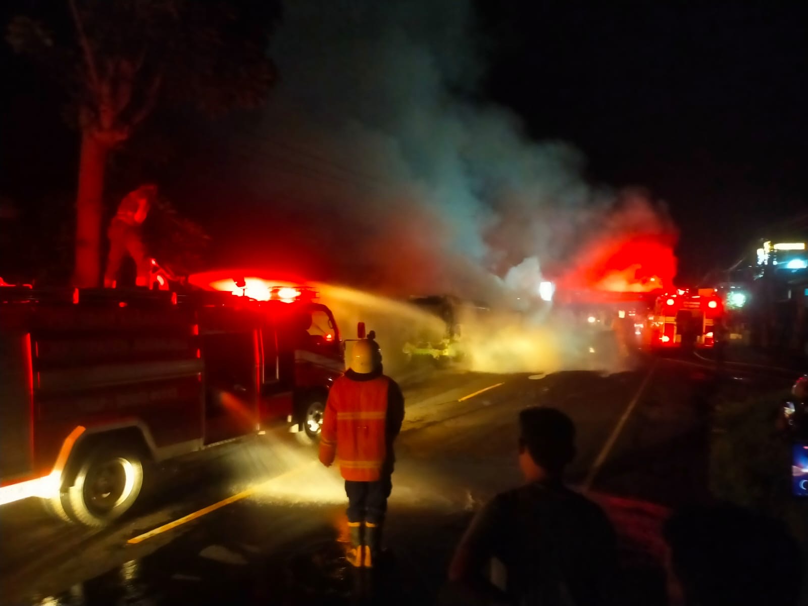 TERBAKAR : Mobil Travel yang terbakar dan api merembet ke tempat usaha potong rambut di Desa Banyubiru, Kecamatan Negara, Jembrana, Minggu (26/1/2025).