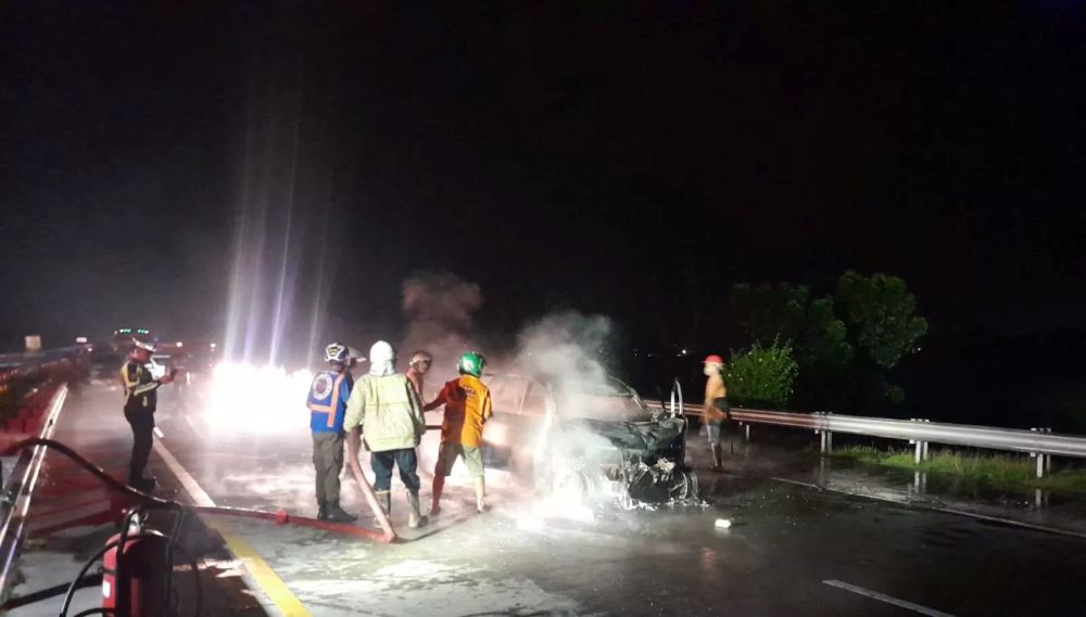 Petugas pemadam kebakaran sedang memadamkan api yang berkobar di seluruh bodi Mobil Avanza  di ruas tol Jombang-Mojokerto.