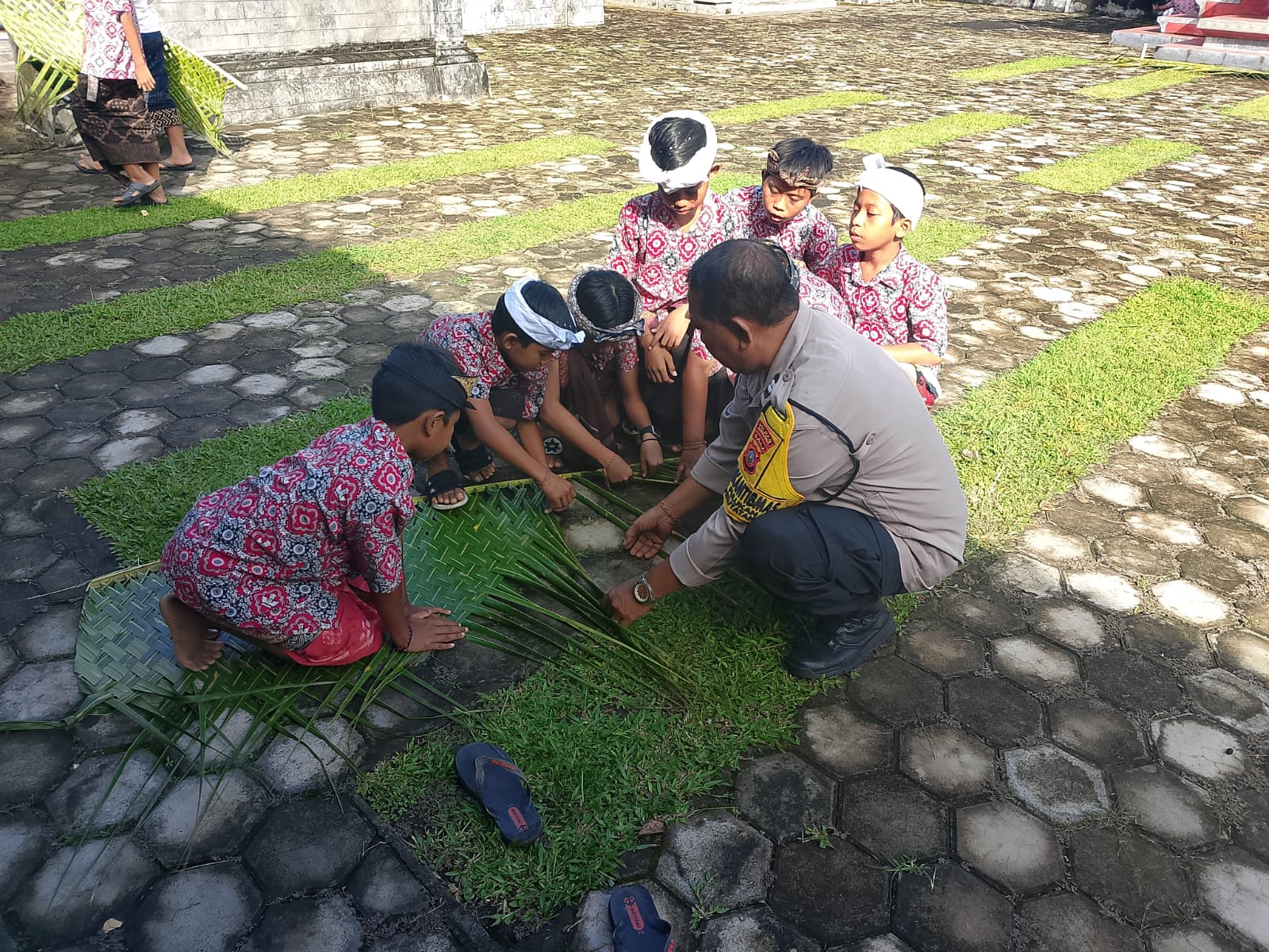 Bhabinkamtibmas Desa Pulukan, Aiptu I Dewa Putu Arta saat mengajarkan anak SD membuat anyaman janur untuk upacara adat, Kamis (28/8).