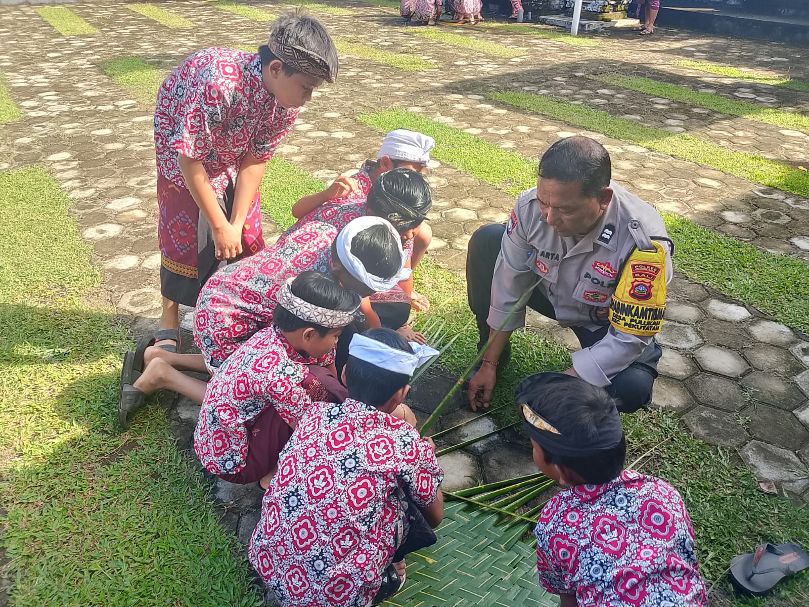 Bhabinkamtibmas Desa Pulukan, Aiptu I Dewa Putu Arta saat mengajarkan anak SD membuat anyaman janur untuk upacara adat, Kamis (28/8).