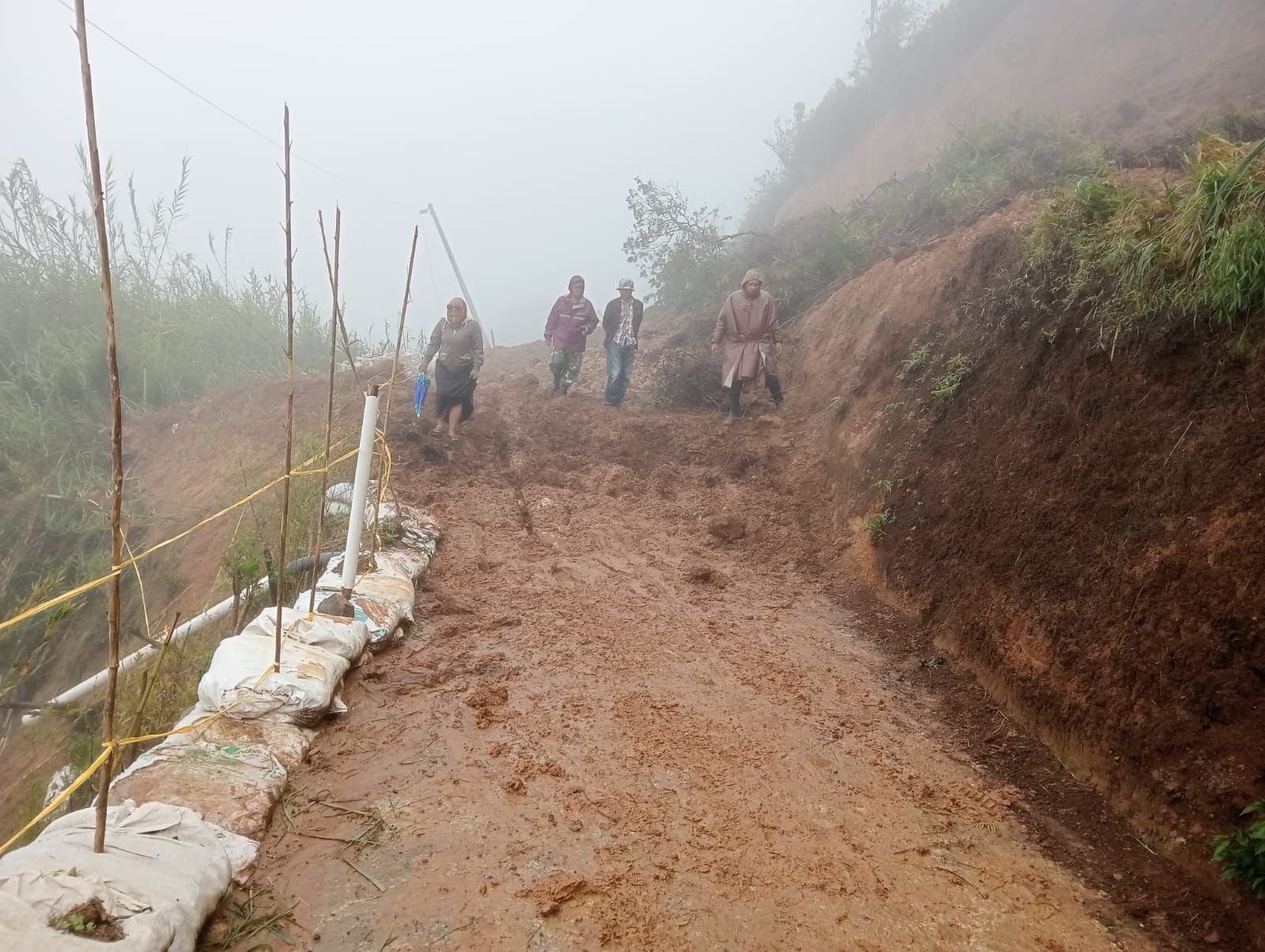 LONGSOR: Petugas bersama warga melewati area longsor di jalan penghubung menuju Gunung Alang. (istimewa)