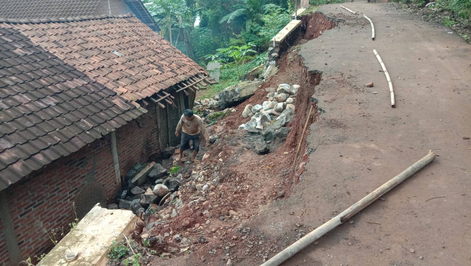 SINGKIRKAN BATU: Junaidi pemilik rumah, sedang menyingkirkan batu, pecahan dari material talud yang longsor. Usai menimpa rumahnya di desa Madugowongjati Gringsing, pada Senin (18/3/2024).