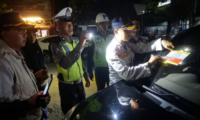 TEMPEL STIKER: Petugas Dishub saat menempelkan stiker pada kendaraan bermotor yang melanggar zona parkir, pada Selasa malam (26/3/2024).