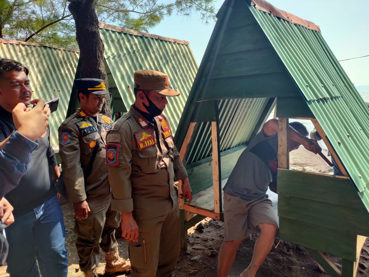 RAZIA: Pemilik warung saat membongkar sendiri dinding yang menutupi gazebo mesum di jalan wisata Pantai Sigandu-Ujungnegoro oleh aparat gabungan Satpol PP, Polres, Kodim 0736 Batang. (Riyan Fadli)