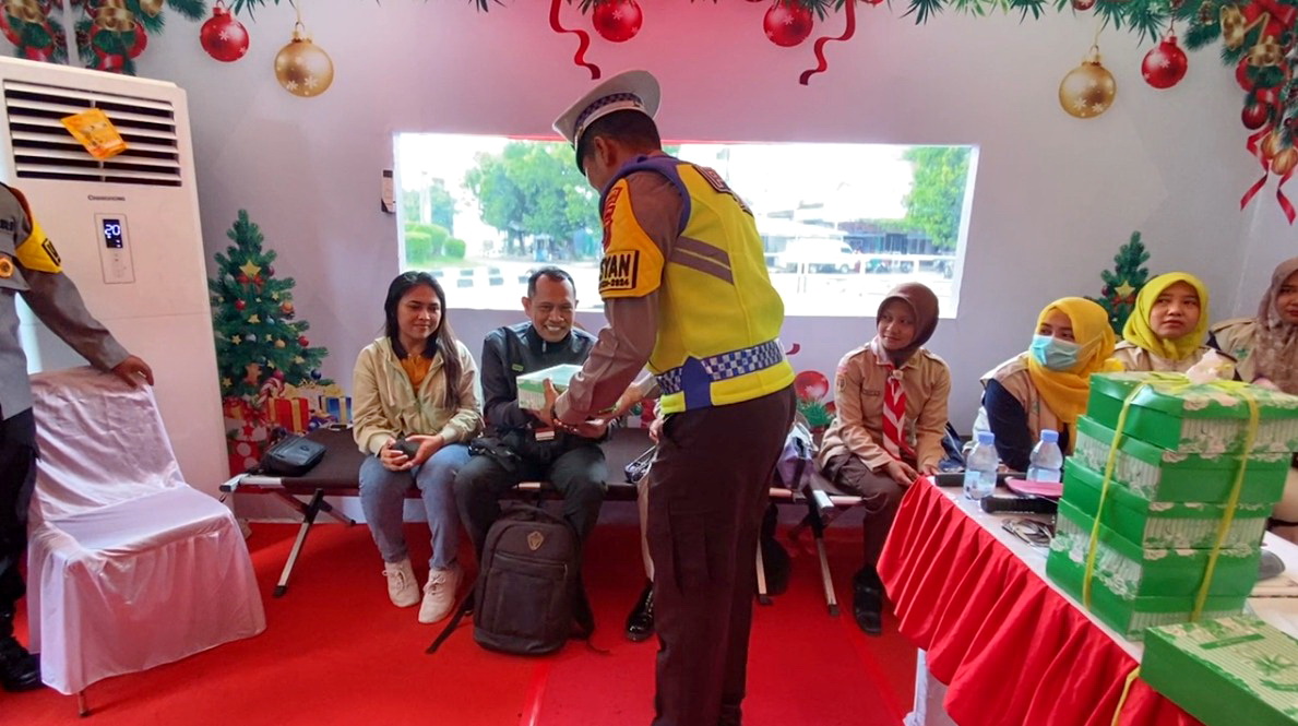 SERAHKAN NASI KOTAK &ndash; Anggota Polres Pemalang saat berikan nasi kotak kepada pemudik yang sitirahat di Pos Alun-Alun Pemalang, pada Senin (23/12/2024).