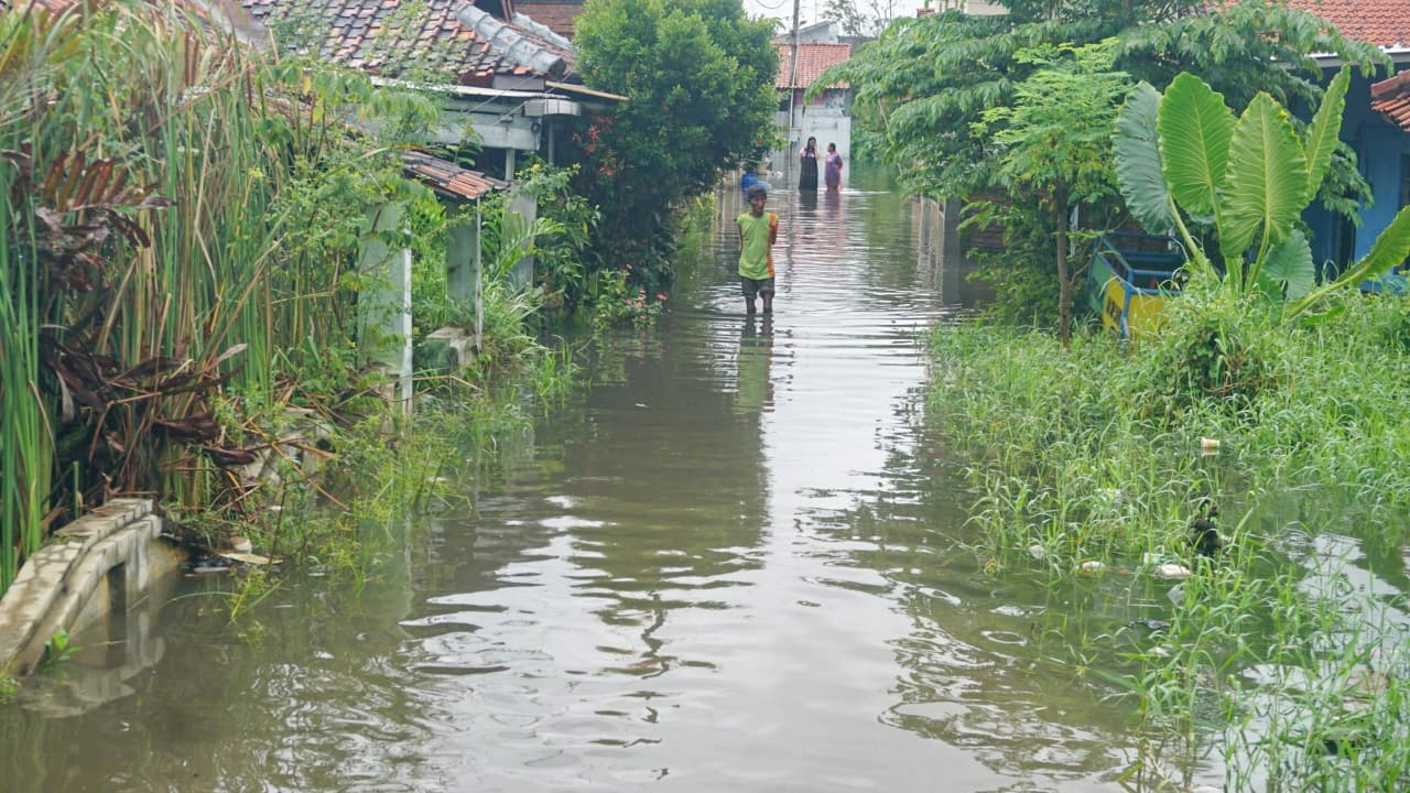 WARGA BERJALAN - Warga Kota Pekalongan saat berjalan melintasi jalan di kampungnya yang terendam banjir, pada Kamis (30/1/2025).