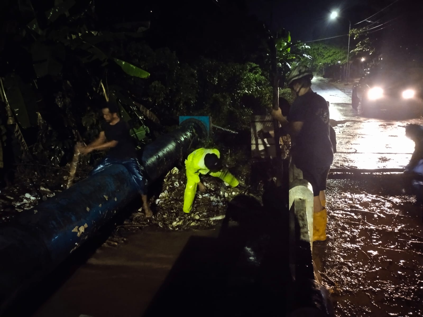 MELUAP: Petugas kepolisian dan relawan Bagana saat berjibaku menormalisasi saluran yang meluap gara-gara tersumbat, Karangdadap, Kabupaten Pekalongan, Selasa (20/1/2026) malam.