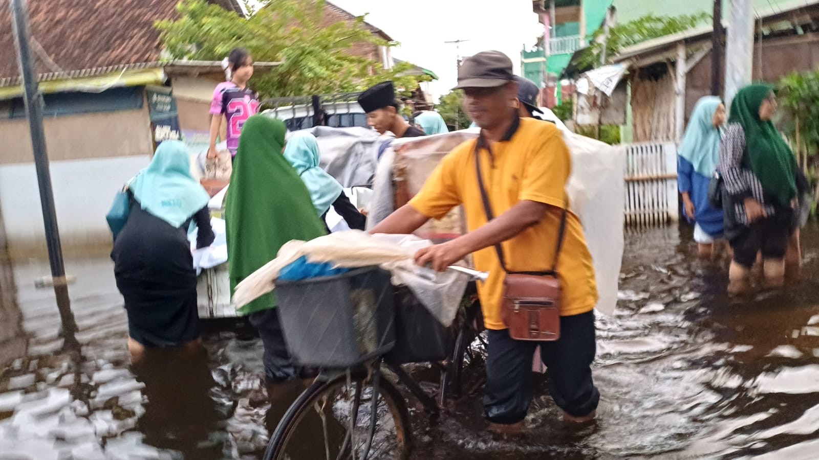 TETAP MENGAIS REZEKI : Seorang bapak tetap berjualan menembus jalanan yang terendam banjir selututnya. Di belakangnya rombongan Annitho Aswaja menyalurkan bantuan,