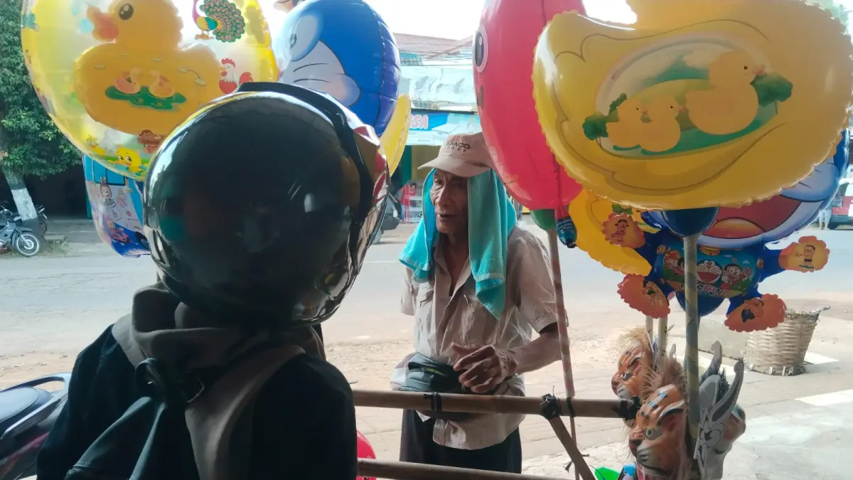 BERJALAN KAKI : Wahidin, 70, menawarkan balon karakter dan topeng kepada pengendara yang berhenti di pinggir jalan kawasan Kajen, Senin 20 Juli 2026. (LAILATUS SYARUFAH/JAWA POS METRO PEKALONGAN)