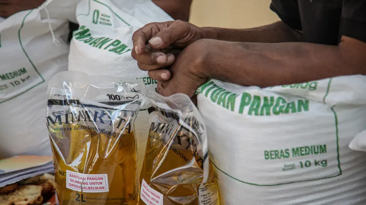 Warga penerima bantuan pangan membawa sejumlah bantuan berupa beras dan minyak goreng saat penyaluran bantuan Keluarga Penerima Manfaat (KPM)  (Hanung Hambara/Jawa Pos)