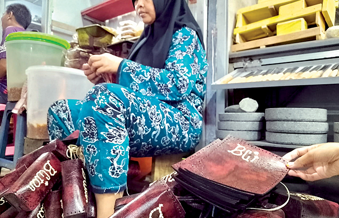CEKATAN: Ismiati ketika membuat dompet kulit sintetis disela-sela berjualan.