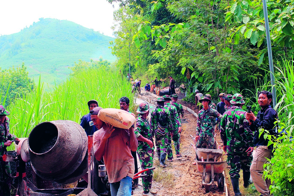 GOTONG-ROYONG: Tentara bersama warga, saling bahu membahu dalam membuat rabat beton.