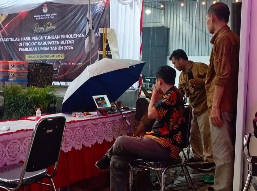 DERAS: Personel KPU memayungi laptop saat rekapitulasi tingkat  kabupaten karena hujan deras.