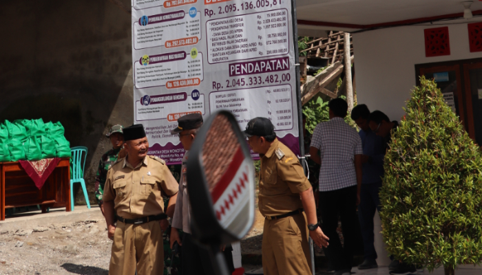 MENUNGGU: Kepala Desa Wonotirto tampak menunggu di bawah baliho transparansi keuangan desanya, kemarin (5/3).