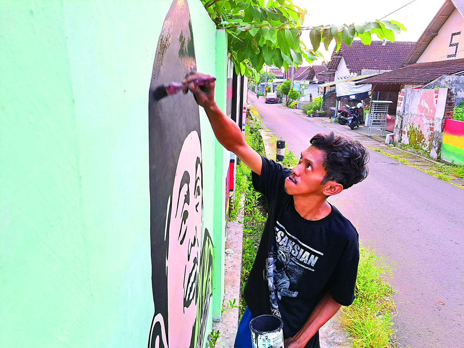 BERJIWA SENI: Abdur Rouf menggoreskan kuas di tembok lingkungan sekitar rumahnya untuk melukis mural, kemarin (15/5).