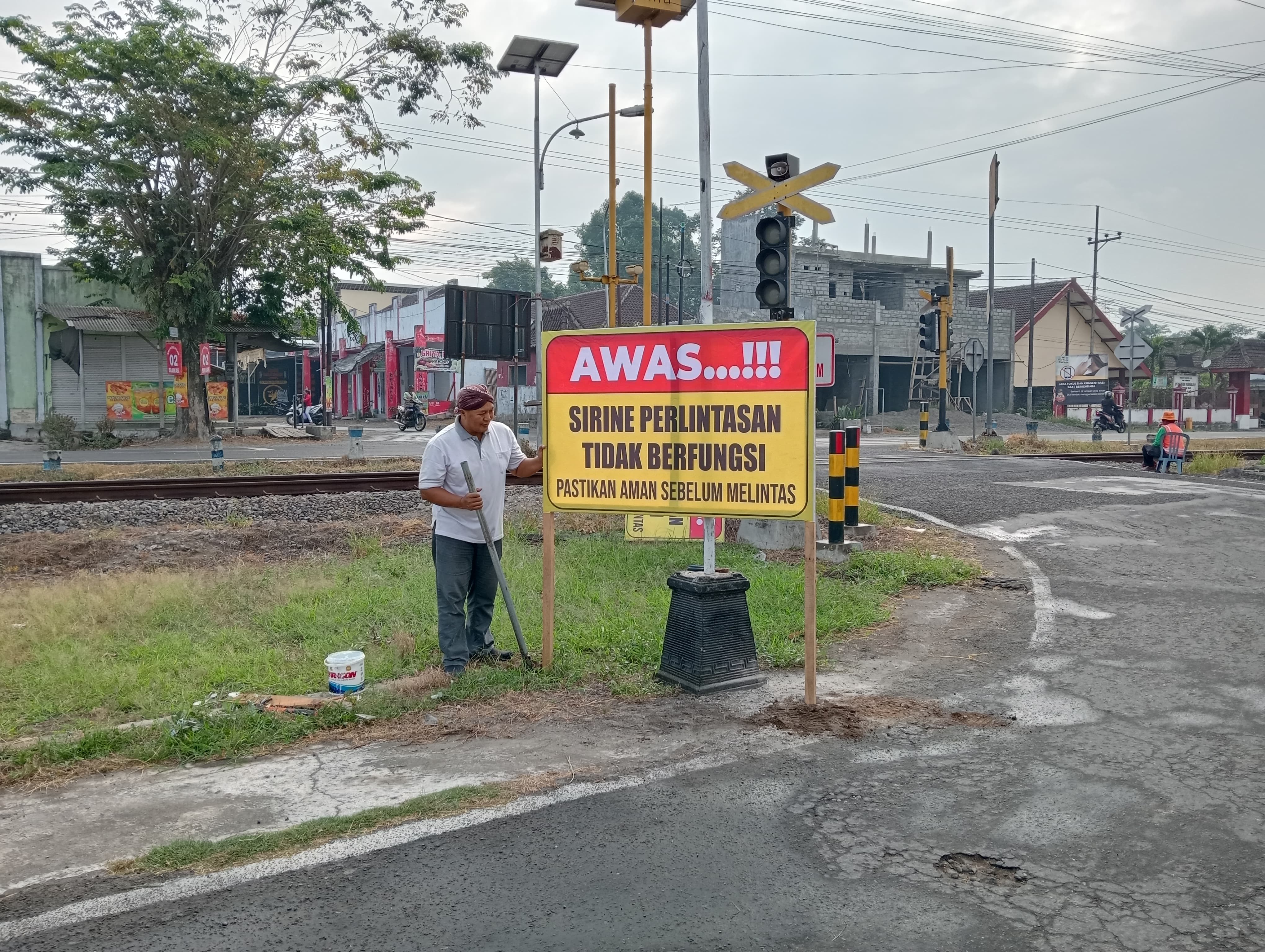 WASPADALAH: Kades Pasirharjo Chusana Churori memasang papan imbauan di perlintasan KA depan Kantor Desa Pasirharjo, Jumat (31/5).
