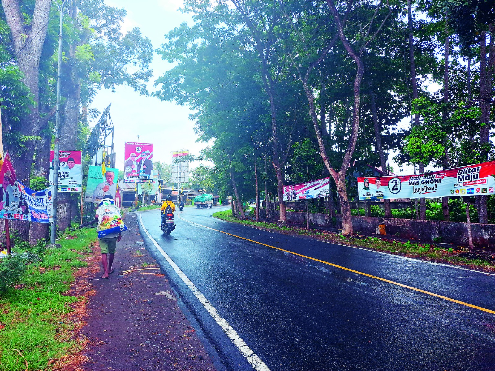 BIJAK MEMILIH: Beberapa  pengendara melintasi APK  fasilitasi KPU Kabupaten Blitar  yang terpasang di Jalan Raya  Garum, Desa Pojok, Kecamatan  Gandusari.